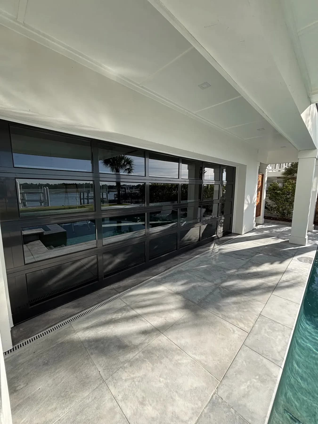 Waterfront home’s covered walkway with a full wall of black-framed glass, pool to one side
